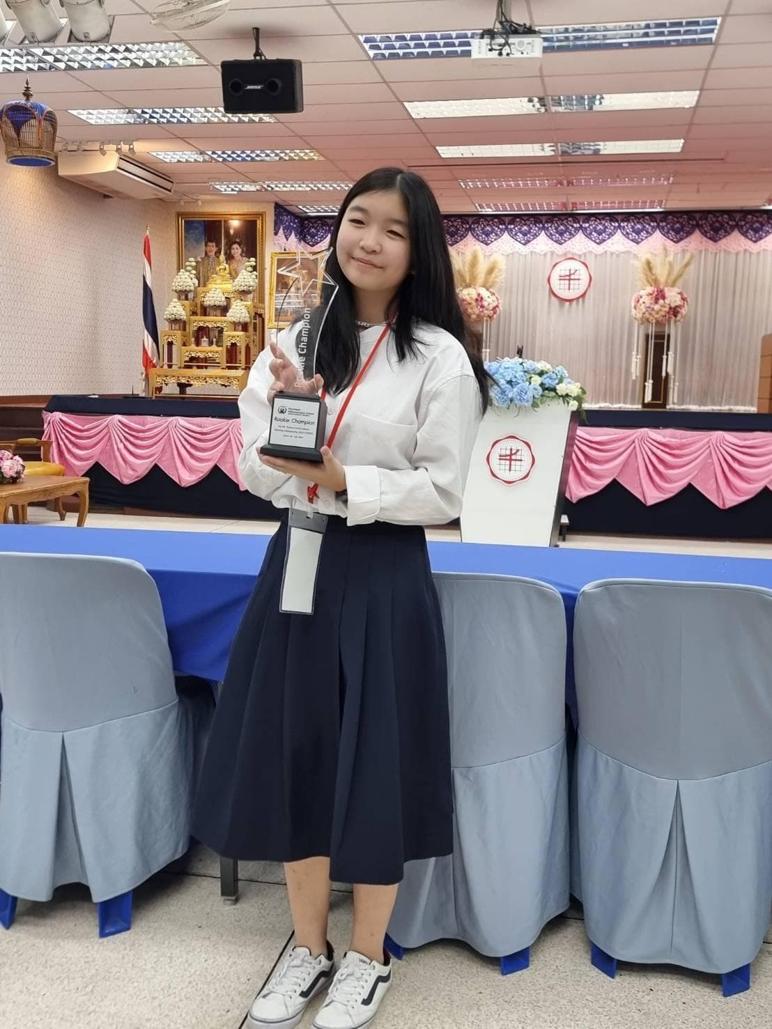 A student holding a Rookie Champion debate trophy at a school ceremony